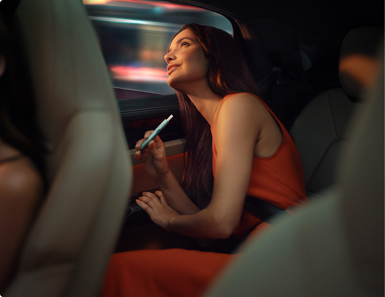 Eine junge Frau mit einem IQOS Gerät in einem Auto.