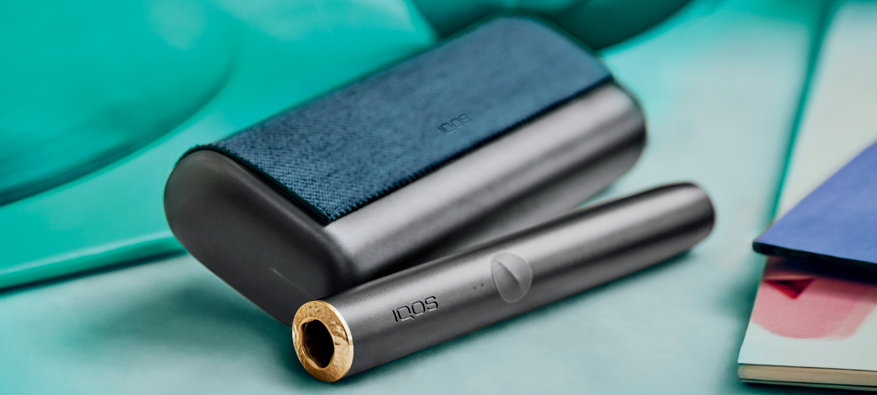 Turquoise IQOS Originals Duo device on a shiny coffee table.