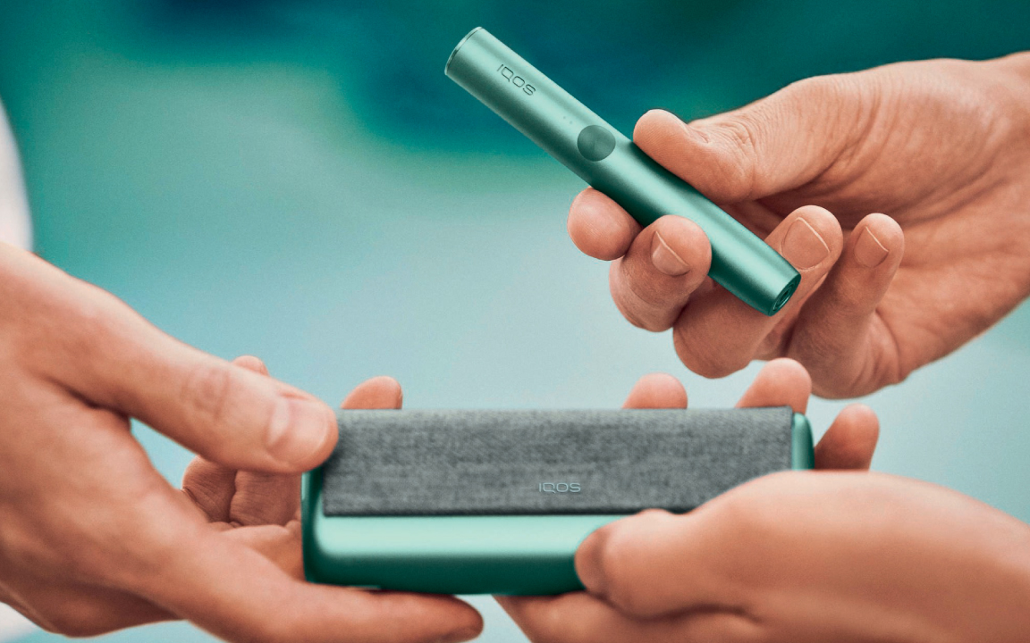 A smiling woman with an IQOS ILUMA device.