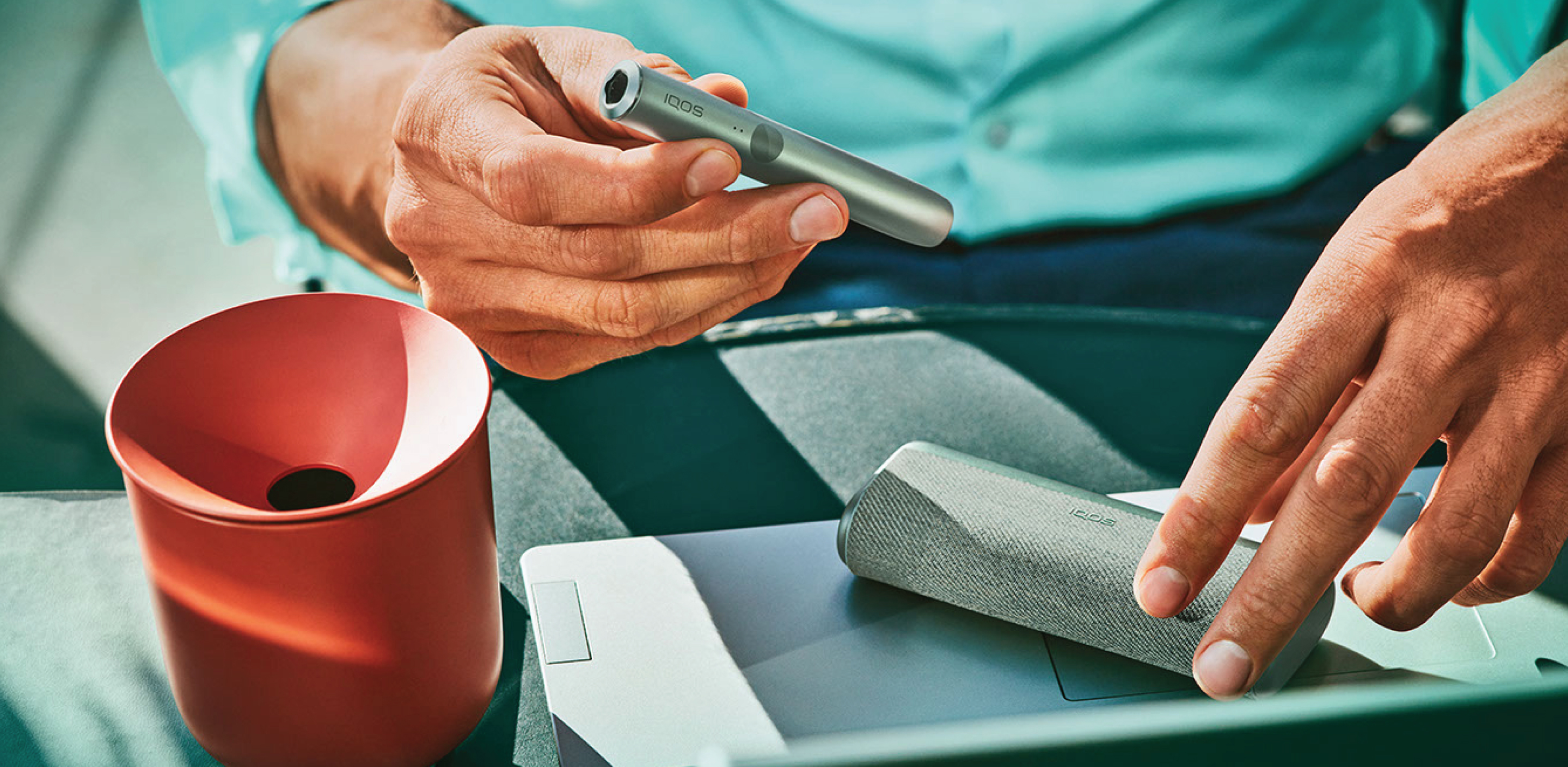 An IQOS device held by one person and a smartphone held by another person.