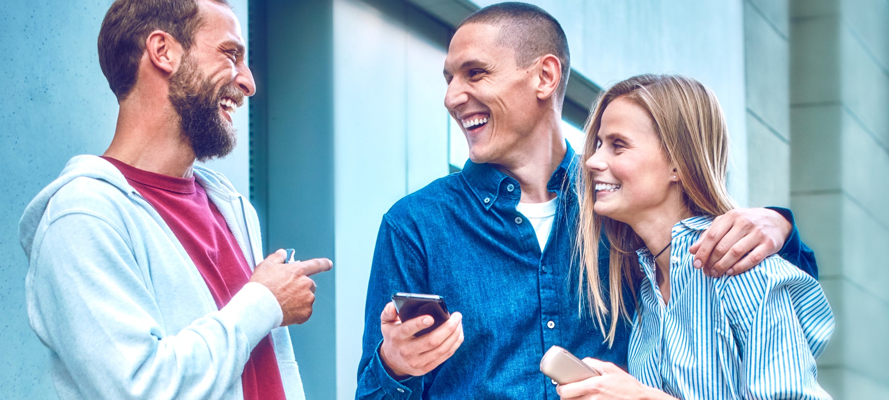 Two people holding IQOS ILUMA devices smile as their friend looks at the IQOS app on her mobile phone.