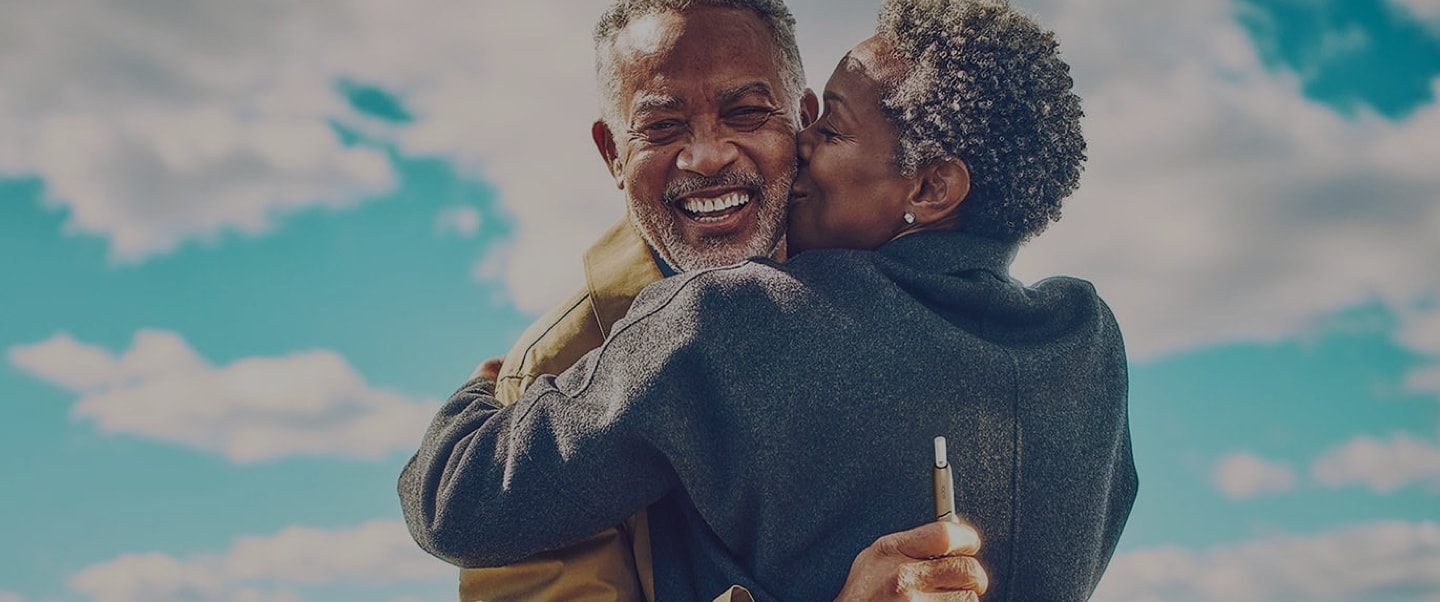 A man holding an IQOS device embraces his partner.