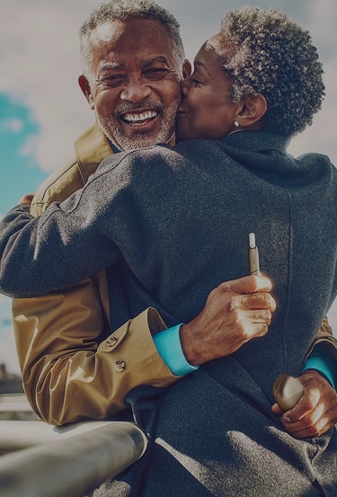 A man holding an IQOS device embraces his partner.