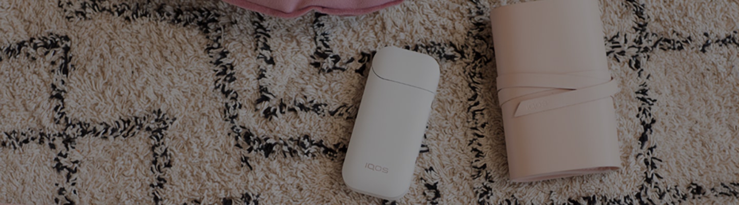 White IQOS 2.4 Plus holder, charger and a pink cover on a carpet 