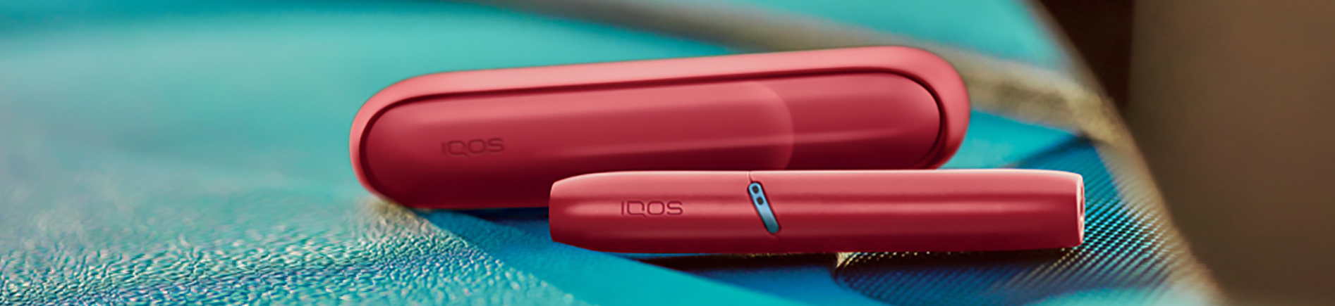Hands holding IQOS Originals Duo heated tobacco holder and pocket charger in turquoise color.