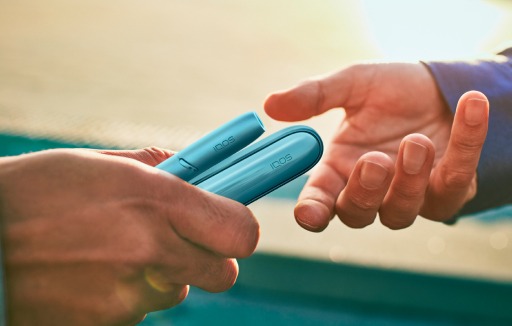 Hands holding a turquoise IQOS Originals Duo heated tobacco device.