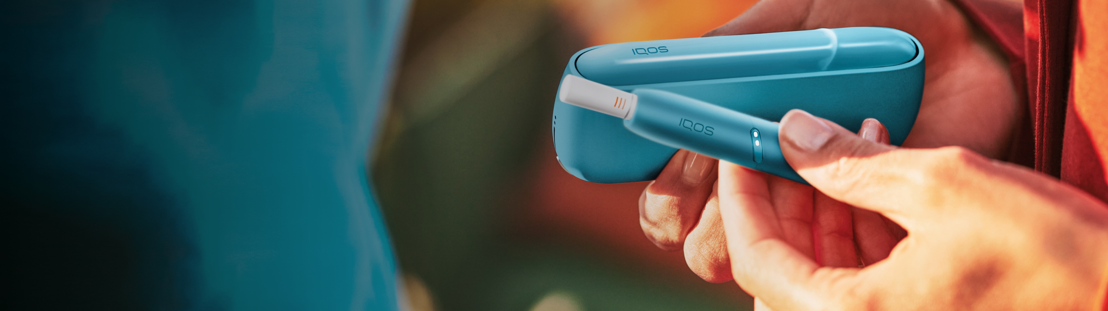 Hände halten ein IQOS Originals Duo in der Farbe türkis