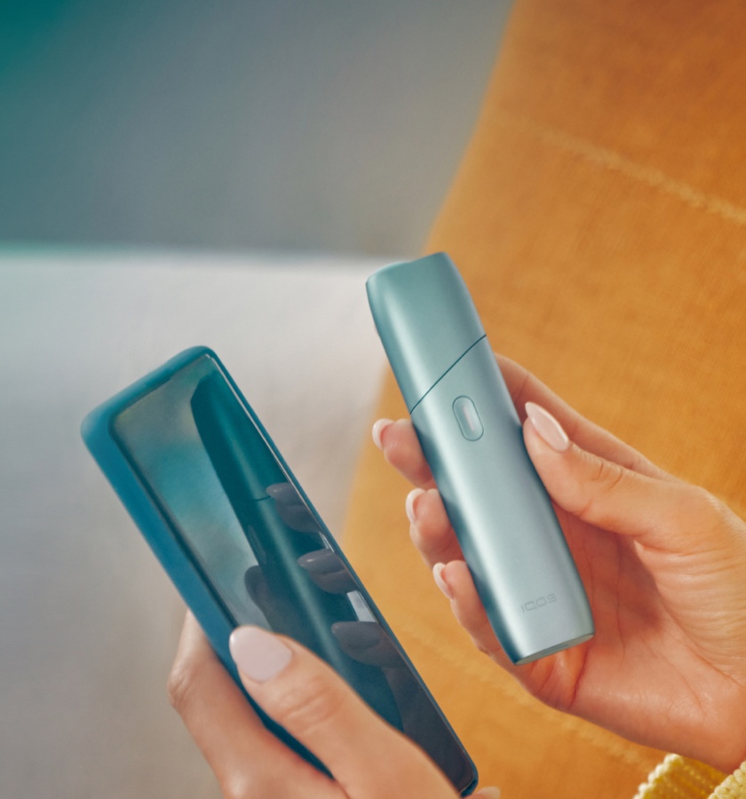 Frau hält einen IQOS Originals ONE Tabakerhitzer und ein Smartphone