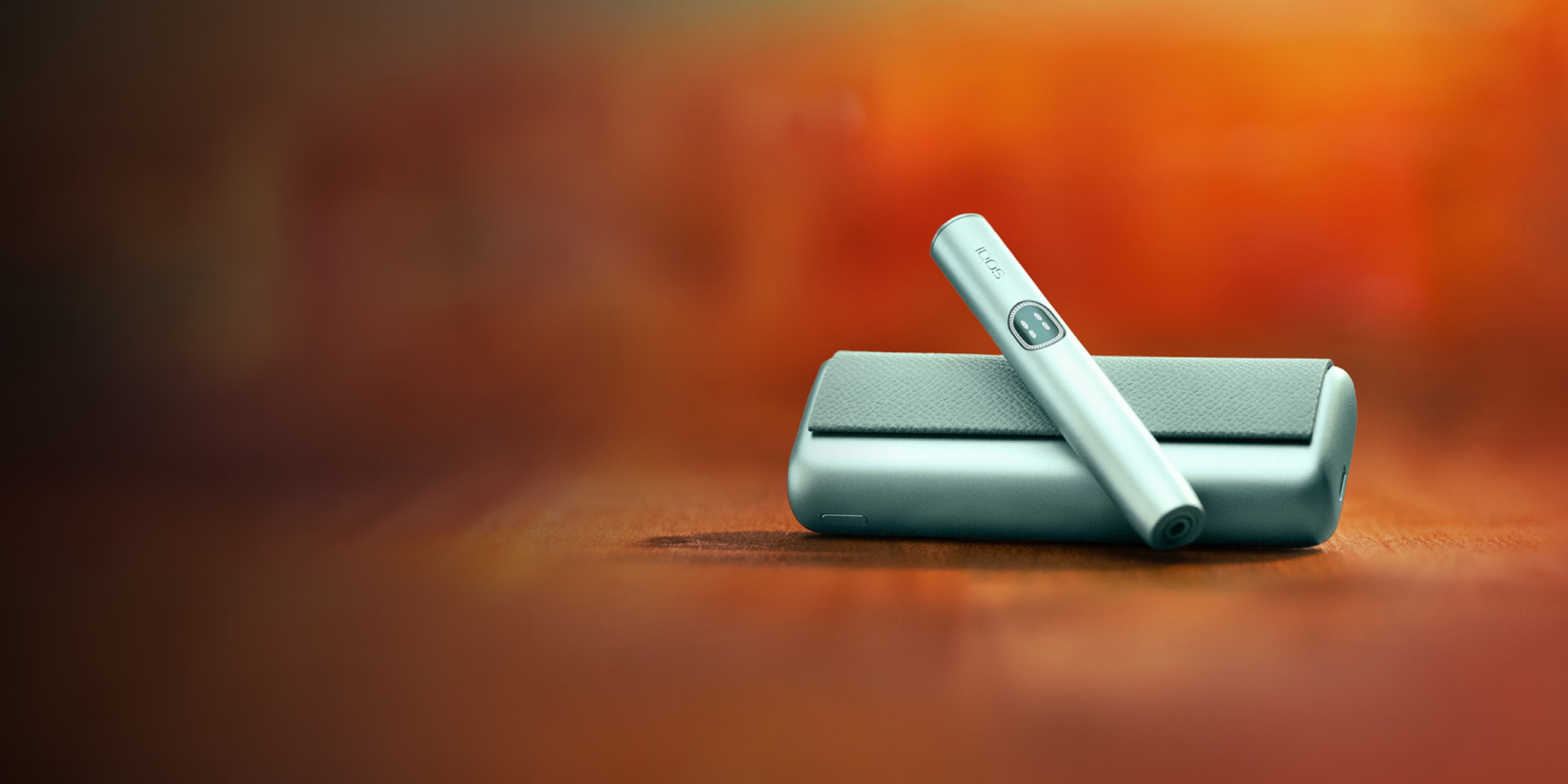 Устройство IQOS ILUMA i PRIME цвета Лазурный бриз над зарядным устройством на красном фоне