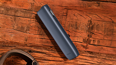 Устройство IQOS ILUMA i ONE цвета Черный графит на деревянном столе