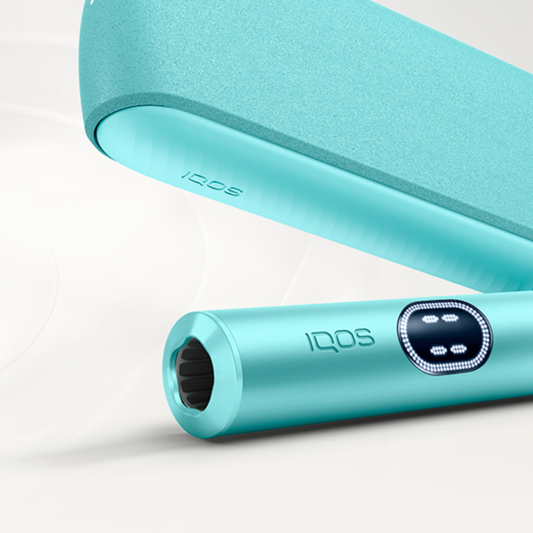 Держатель IQOS ILUMA i цвета Лазурный бриз лежит перед зарядным устройством на сером фоне