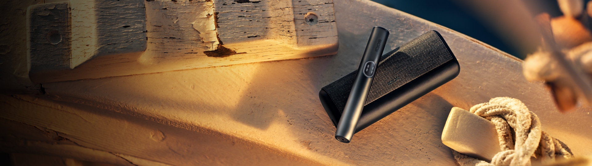 Устройство IQOS ILUMA i PRIME цвета Черный графит над зарядным устройством на белой поверхности