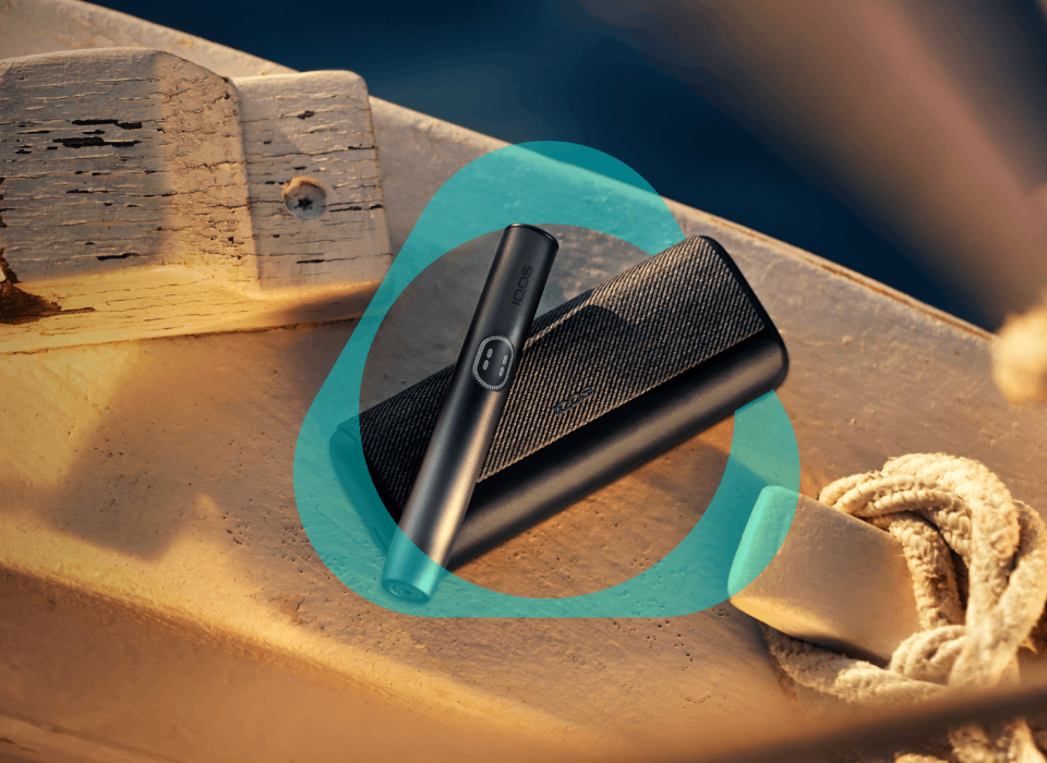 Держатель IQOS ILUMA i PRIME цвета Черный графит внутри логотипа IQOS на белой деревянной поверхности