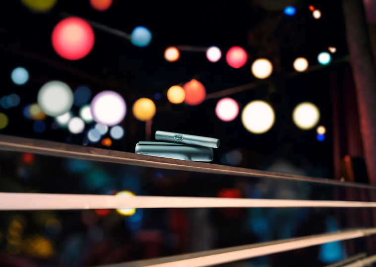 Устройство IQOS ILUMA i PRIME цвета Лазурный бриз на перилах на светлом фоне