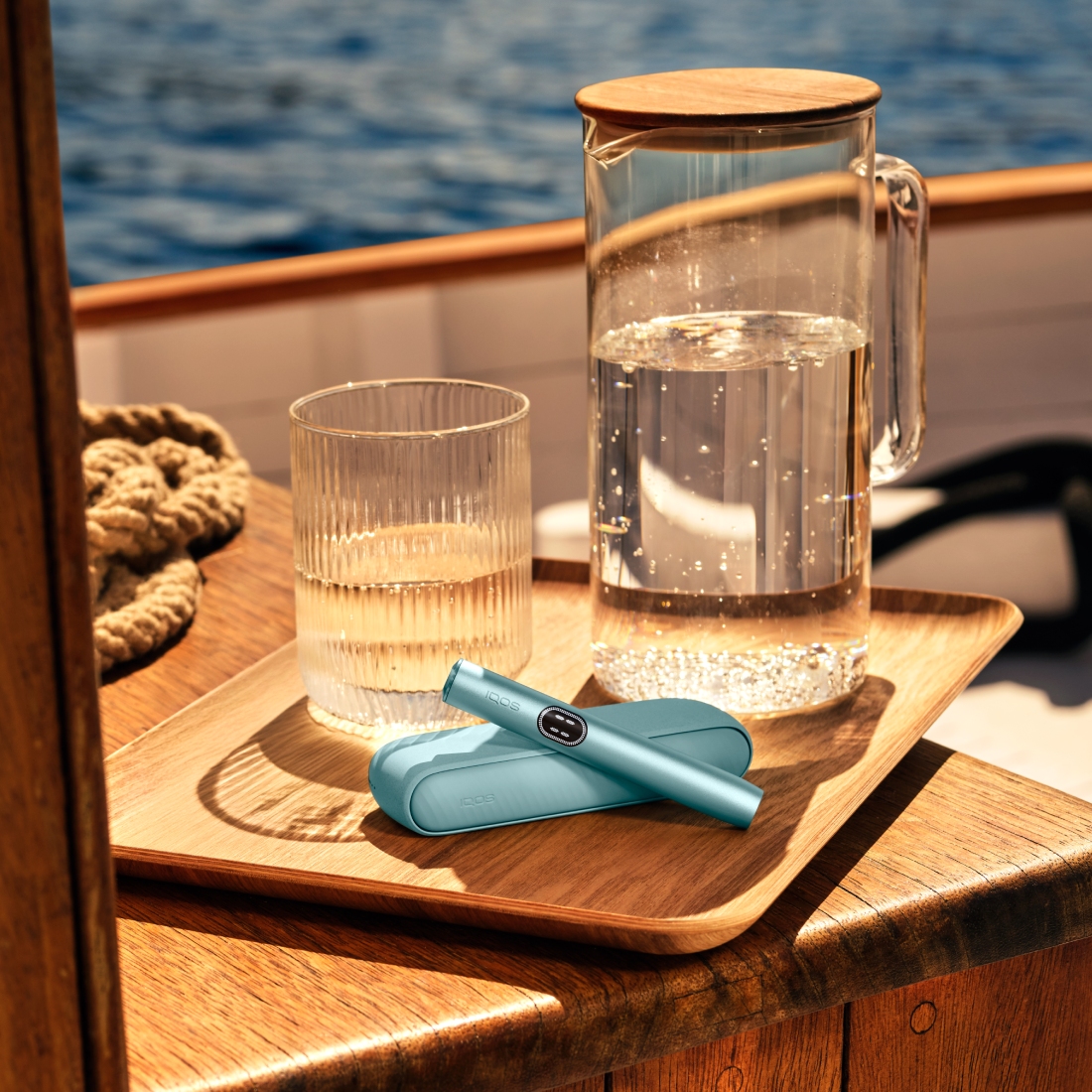 Устройство IQOS ILUMA i PRIME цвета Лазурный бриз над зарядным устройством на деревянной доске