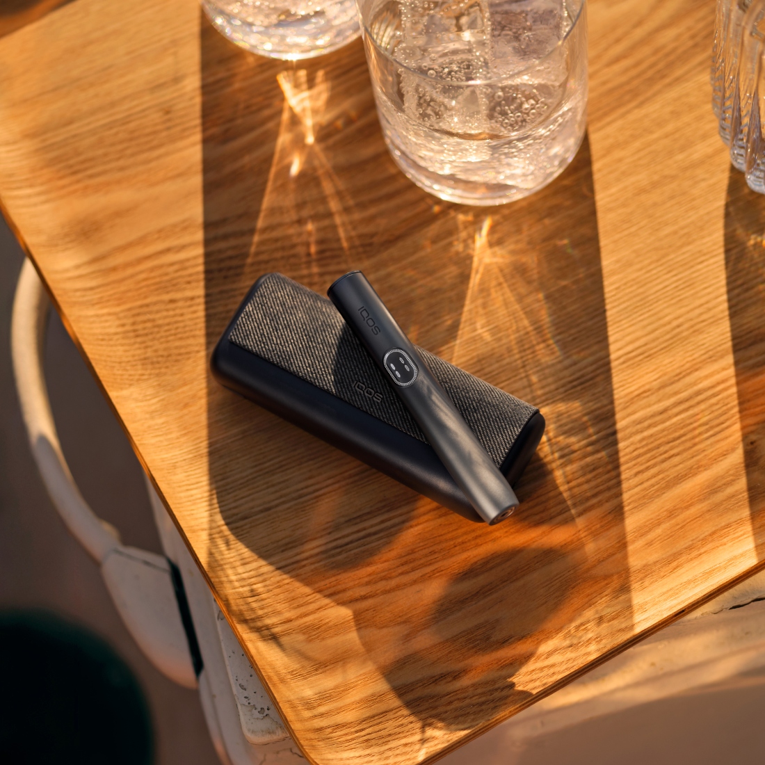 Устройство IQOS ILUMA i PRIME цвета Черный графит над зарядным устройством на деревянной доске