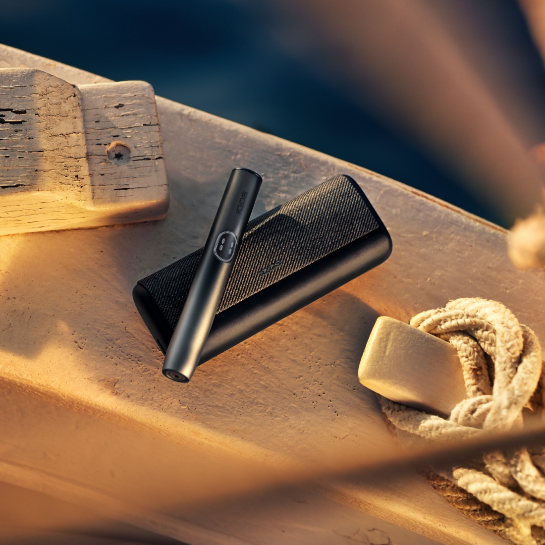 Устройство IQOS ILUMA i PRIME цвета Черный графит над зарядным устройством на белой поверхности