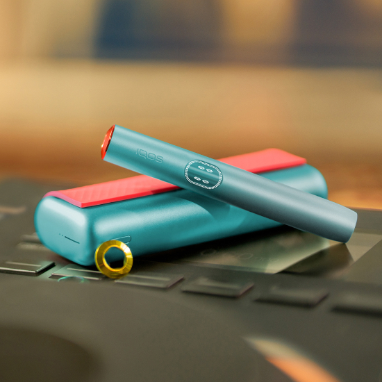 Blue IQOS ILUMA i PRIME device above its charger, customized with wrap and rings