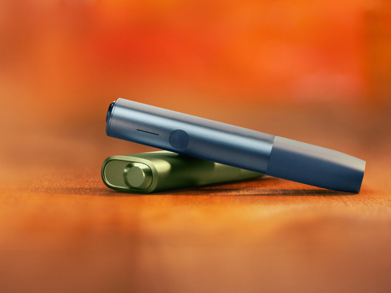 Blue IQOS ILUMA i ONE above a green IQOS ILUMA i ONE, with red background