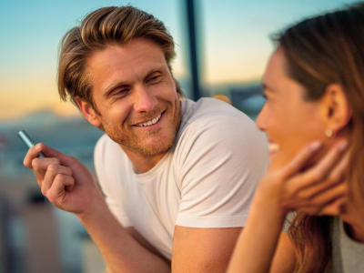 Two people smiling while holding an IQOS ILUMA i PRIME device