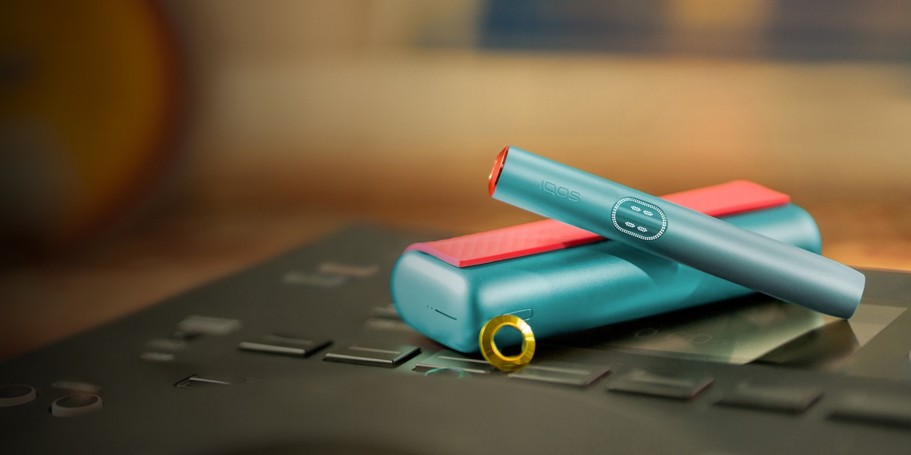 Blue IQOS ILUMA i PRIME device above its charger, customized with wrap and rings