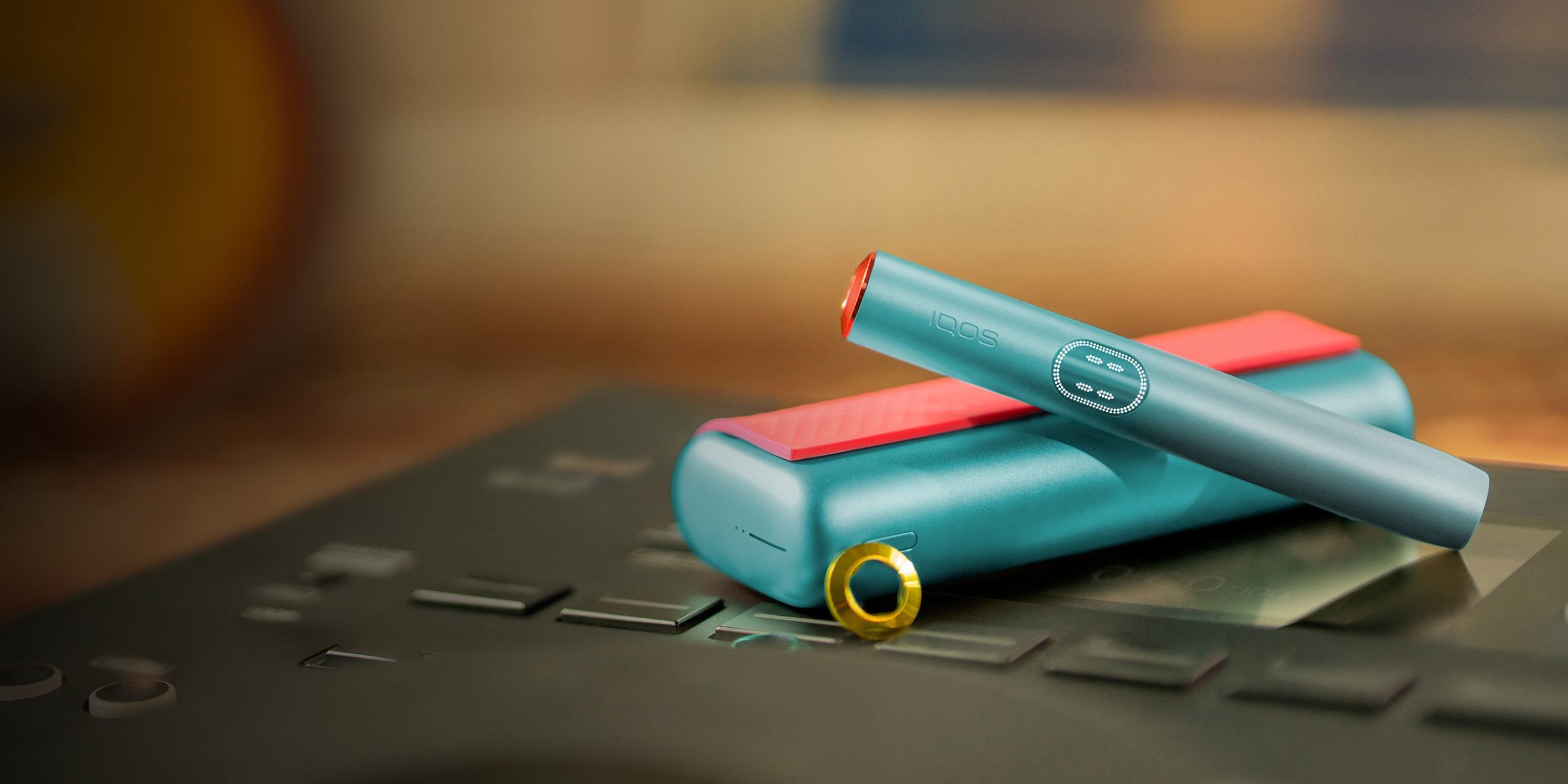 Blue IQOS ILUMA i PRIME device above its charger, customized with wrap and rings