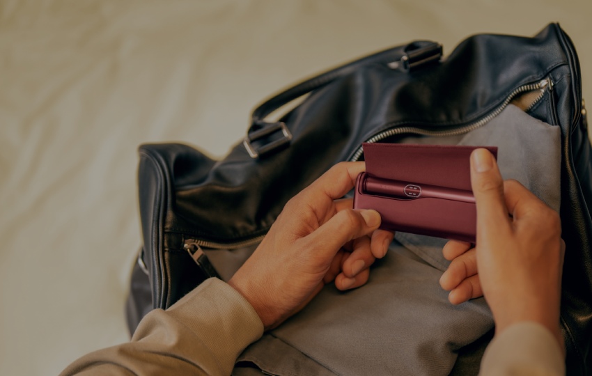 A person interacting with IQOS device in a casual indoor setting.