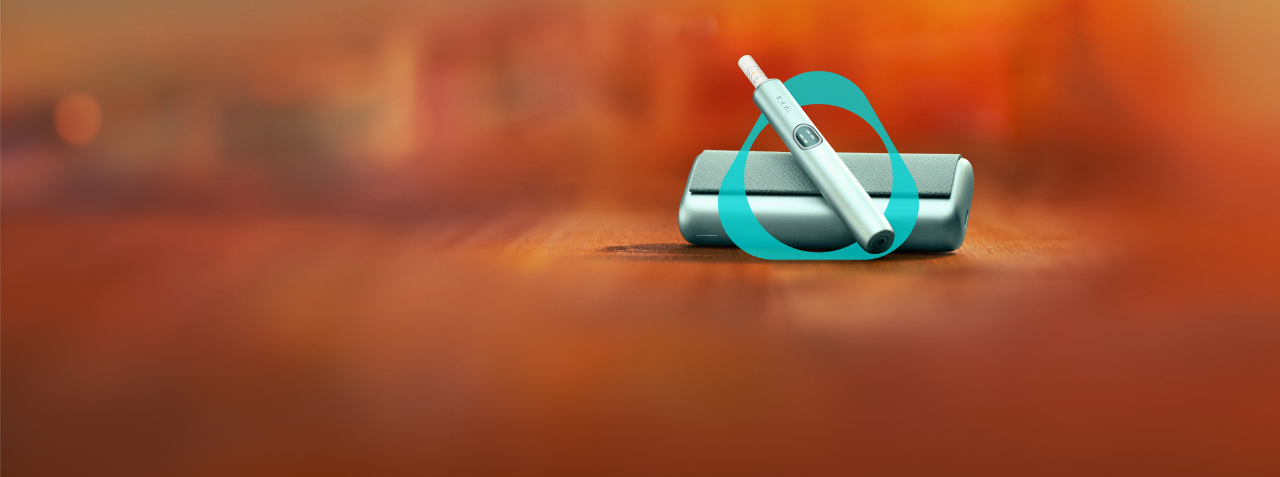 Close-up of an IQOS ILUMA i PRIME with a TEREA stick inserted on its holder. The holder is resting on top of its pocket charger, set against a warm orange-red gradient background.