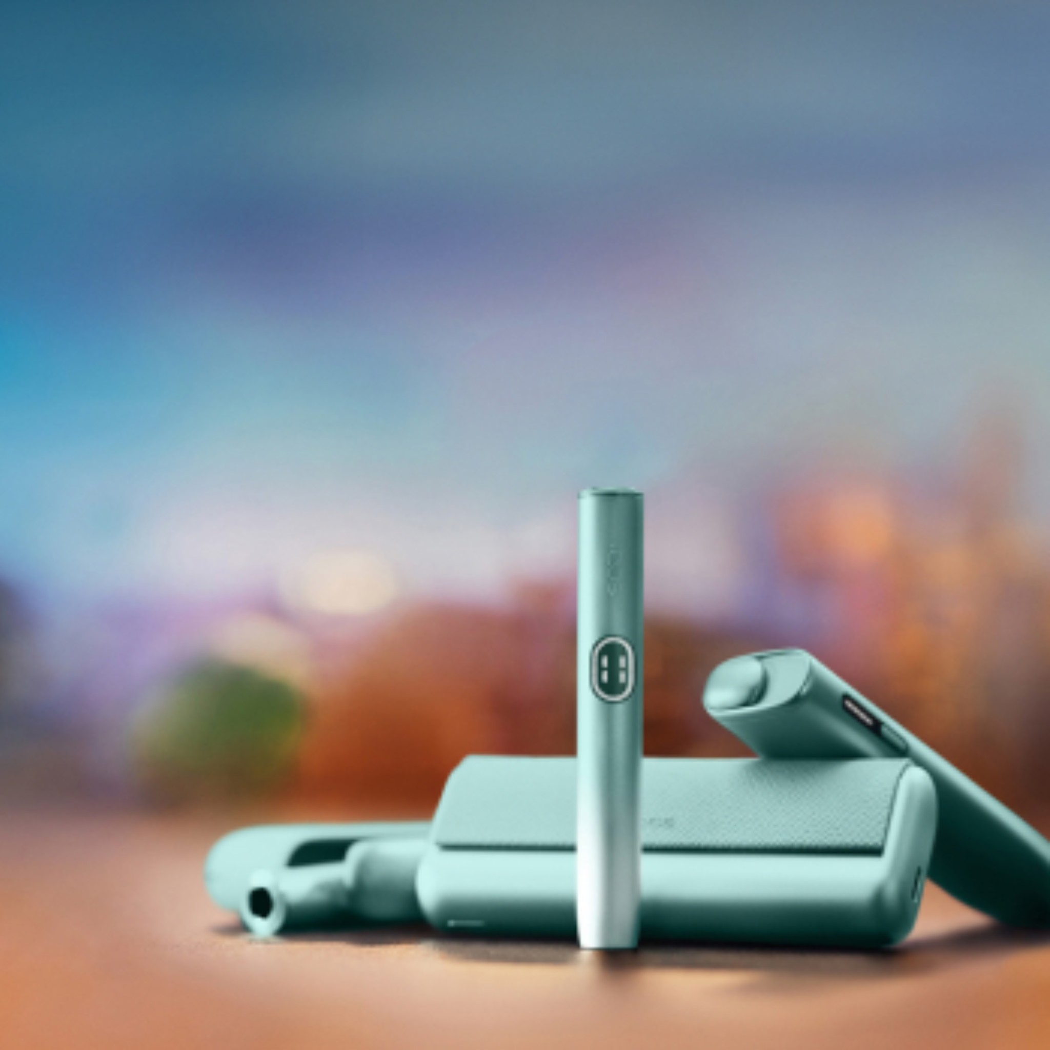 The IQOS ILUMA i range of devices in Breeze Blue against a soft pastel background with blurred shades of blue, purple, and green creating a calm, modern aesthetic.