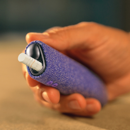 Hand holding an IQOS ILUMA i ONE device with violet sleeve