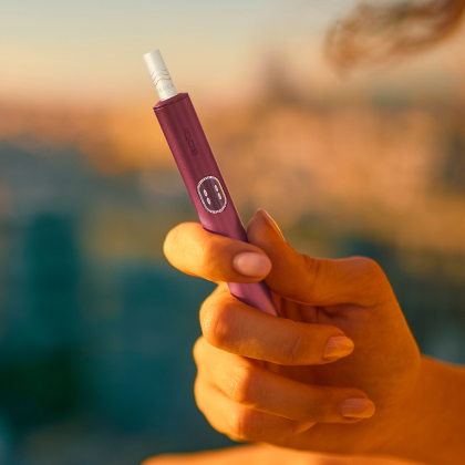 Hand holding a Garnet Red IQOS ILUMA i PRIME device