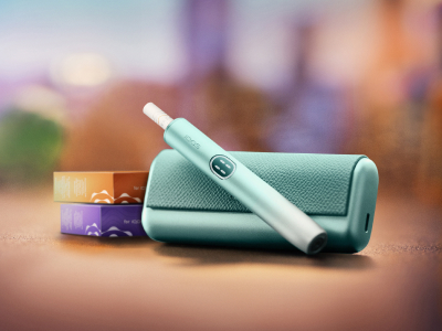 Breeze Blue IQOS ILUMA i PRIME device above its charger, near two packs of consumables