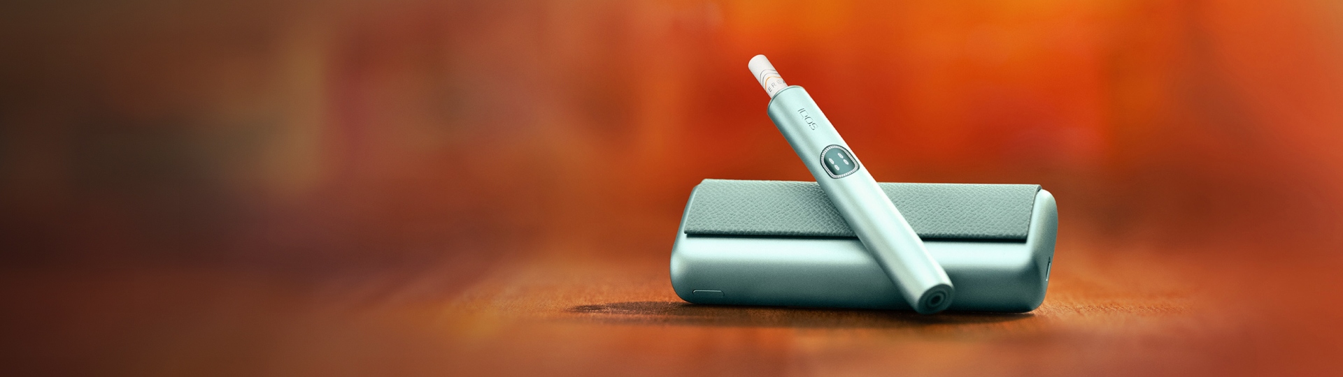 Green IQOS ILUMA i PRIME device above its charger, with red background