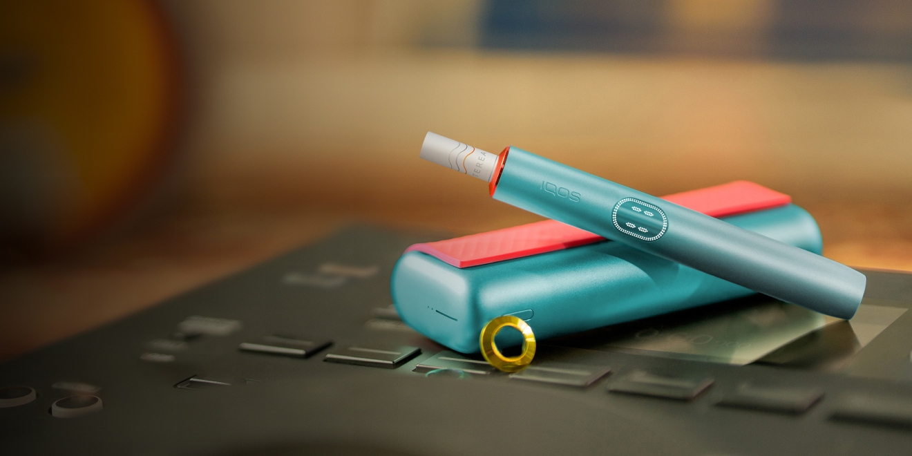Blue IQOS ILUMA i PRIME device above its charger, customized with wrap and rings