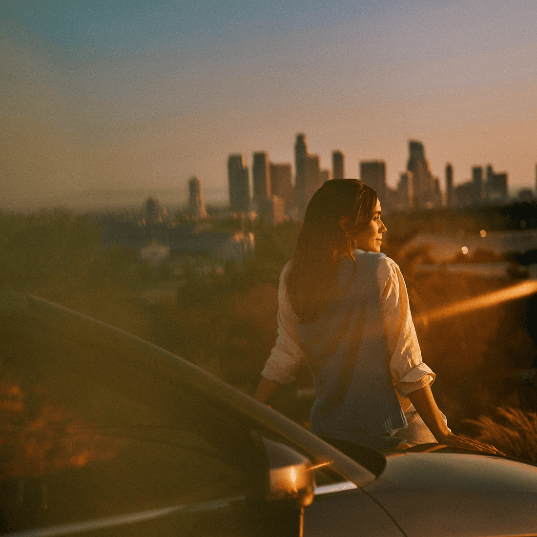 A woman reclining on a car while watching the sunset