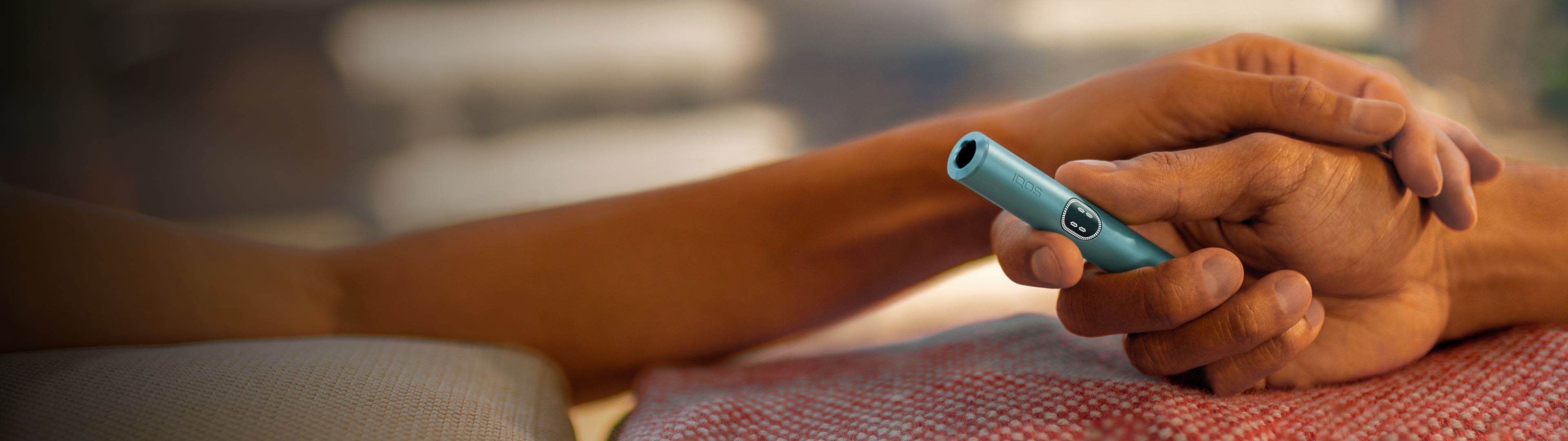 Zwei Hände halten sich, eine davon hält ein IQOS ILUMA i Gerät in der Farbe Breeze Blue.