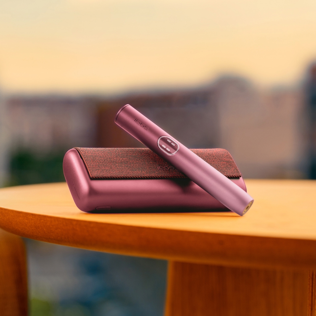 Устройство IQOS ILUMA i PRIME гранатово-красного цвета над зарядным устройством, на столе