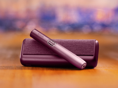 Устройство IQOS ILUMA i PRIME гранатово-красного цвета над зарядным устройством