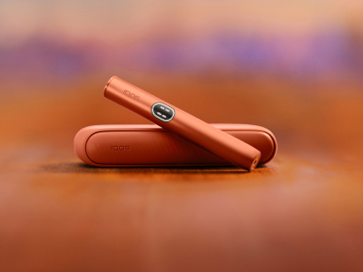 Устройство IQOS ILUMA i терракотового цвета над зарядным устройством на красном фоне