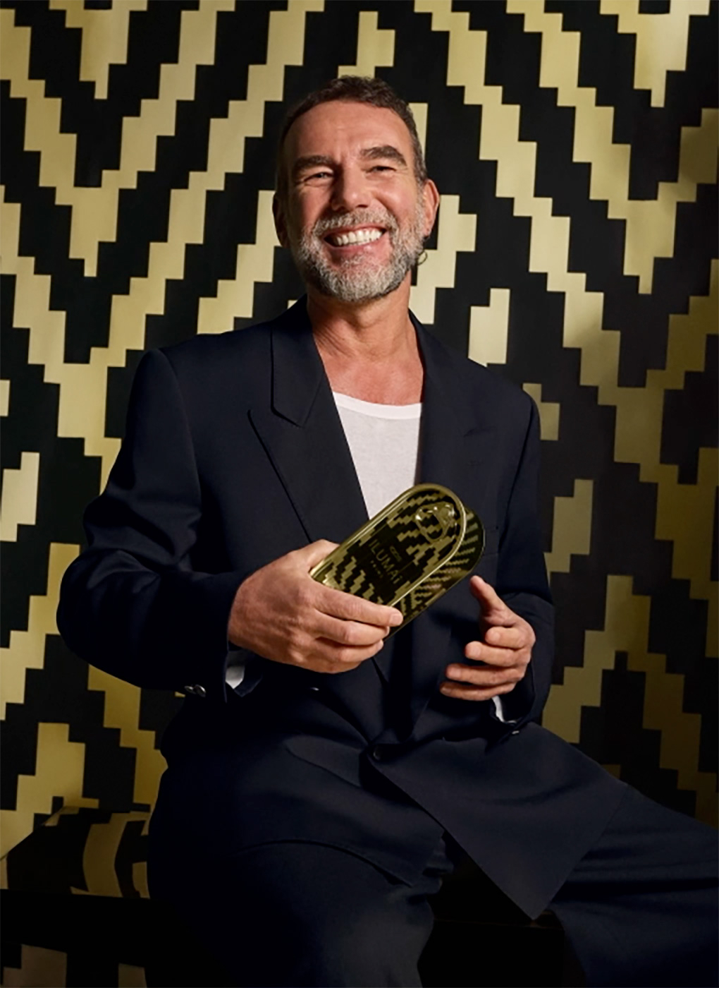 Fotka italského designéra Stefana Selettiho, který se umívá a v pravé ruce drží jeden ze svých návrhů; za ním je černo-zlaté pozadí.