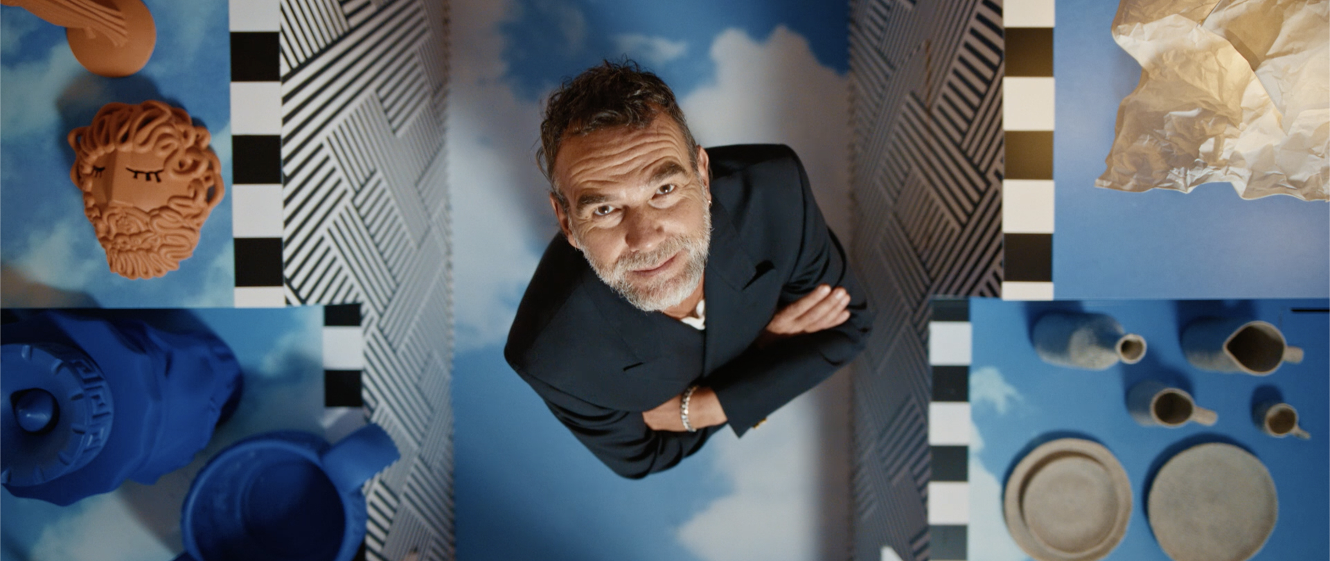 Italský designér Stefano Seletti zachycen na fotce, kdy fotoaparát na něj míří z vrchu a kolem jsou vidět jeho návrhy produktů.