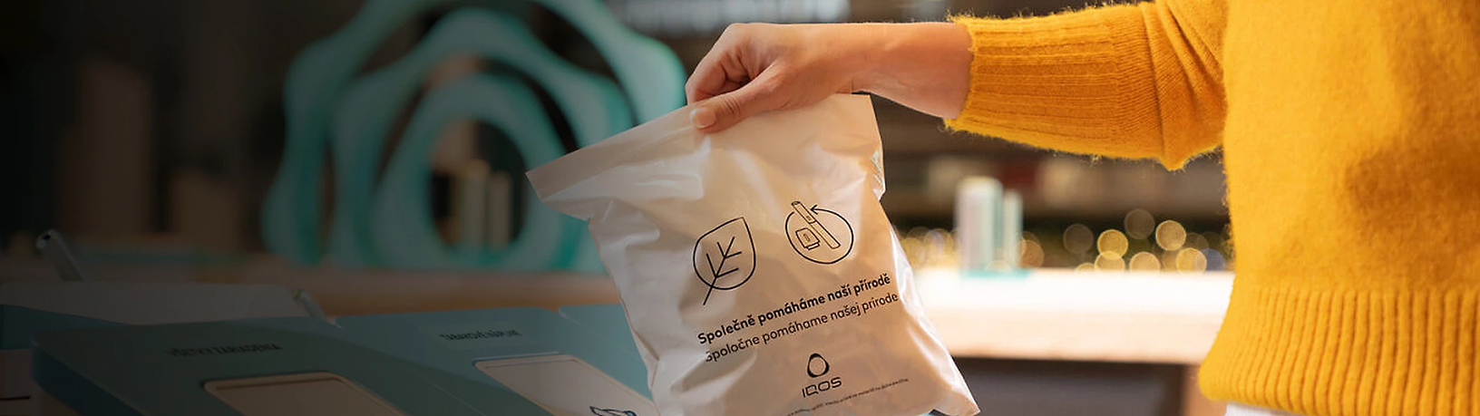 Žena v oranžovém svetru vhazující do recyklačního boxu plný sáček IQOS