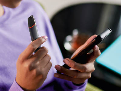 Ruce držící black VEEV inPRIME vaping zařízení a telefon