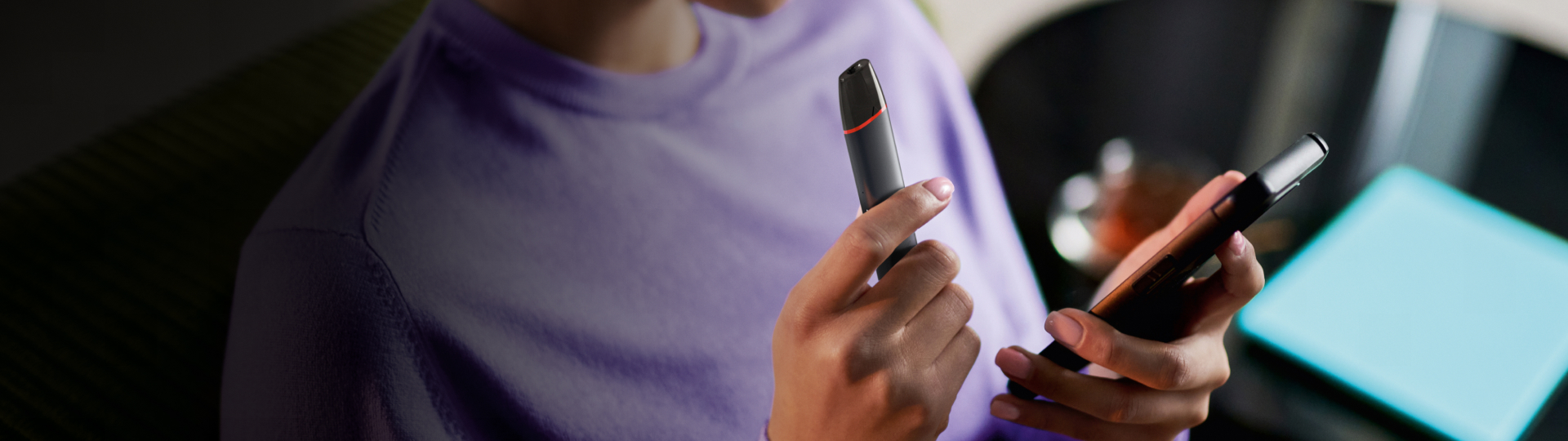 Ruce držící black VEEV inPRIME vaping zařízení a telefon