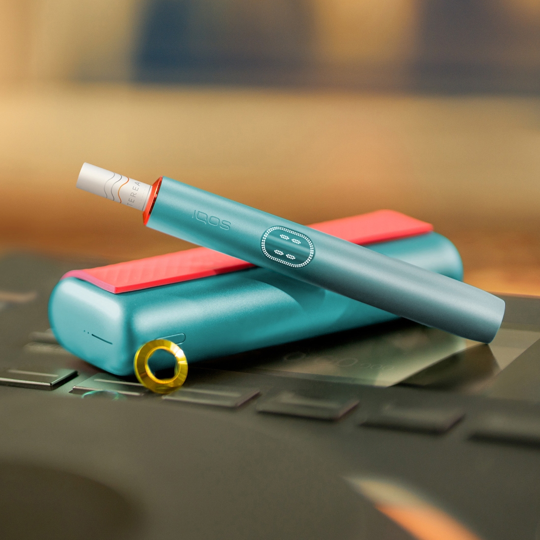 Blue IQOS ILUMA i PRIME device above its charger, customized with wrap and rings