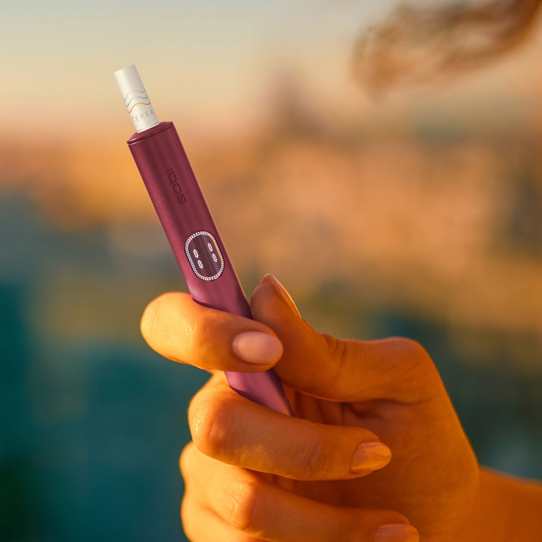 Hand holding a Garnet Red IQOS ILUMA i PRIME device