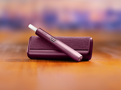 Garnet Red IQOS ILUMA i PRIME device above its charger