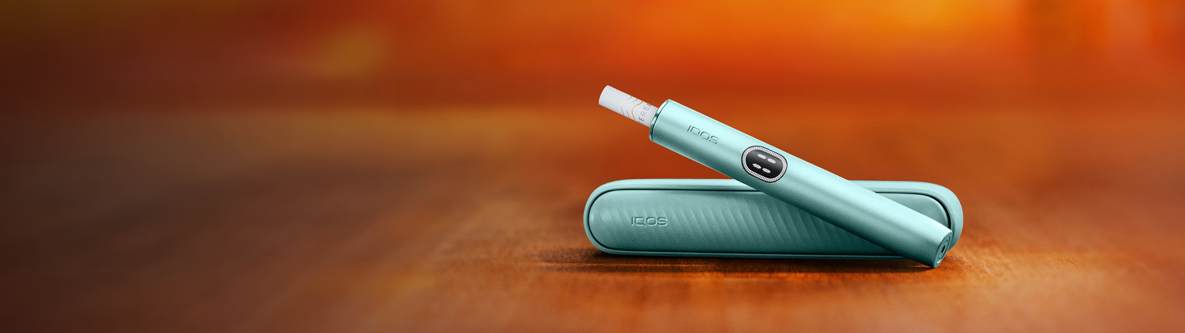 جهاز IQOS ILUMA i باللون الأزرق السماوي فوق الشاحن الخاص به، بخلفية حمراء
