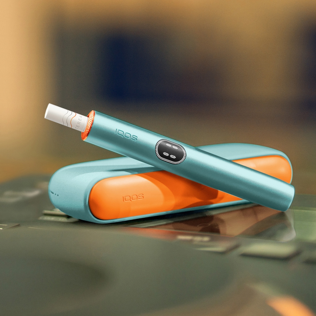 جهاز IQOS ILUMA i ذو اللون الأزرق السماوي فوق الشاحن الخاص به، مع باب وحلقات مخصصة
