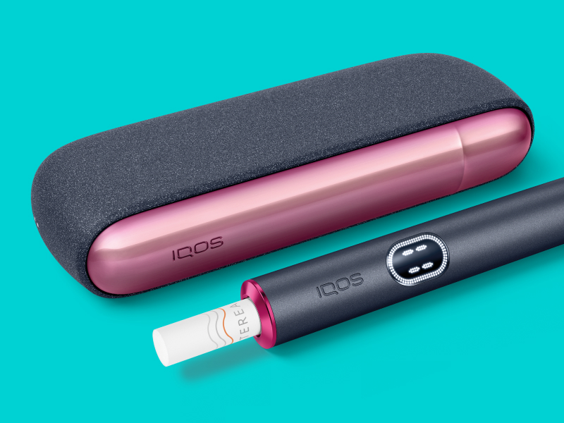جهاز IQOS ILUMA i بالقرب من شاحنه، مع باب وحلقة مُصممين خصيصًا.